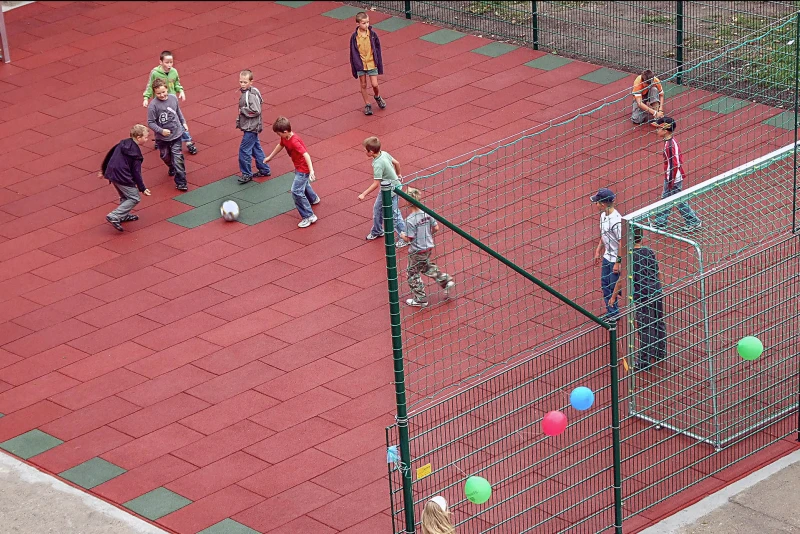 I bambini giocano a calcio sul nuovo campo da calcio realizzato con il pavimento di gomma rossa e verde di WARCO.