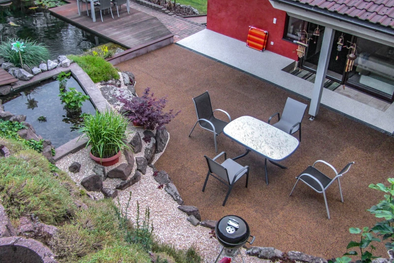 Eine idyllische Wohlfühloase für die Familie zwischen Hang und Haus. Eine großzügige Terrasse aus WARCO-Platten und ein naturnaher Teich laden zum Verweilen ein. Die üppig bewachsene Böschungssicherung umrahmt die Familienoase.
