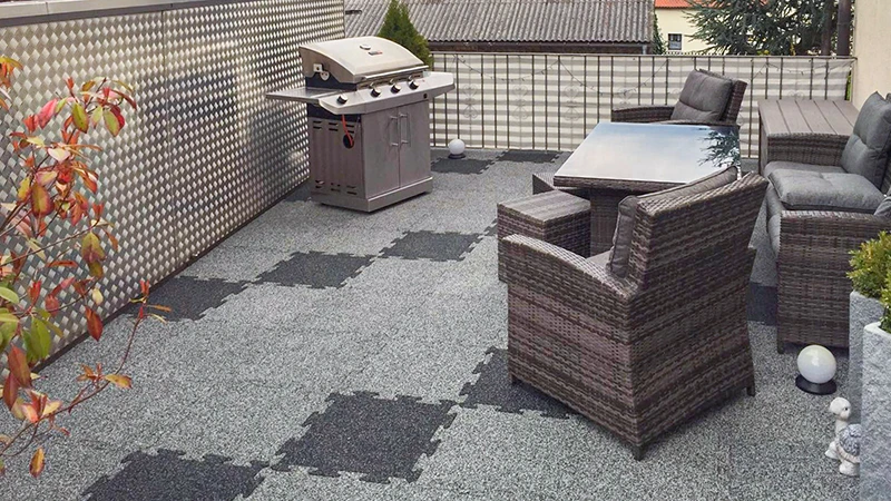 Auf dem Foto sieht man eine geräumige Dachterrasse mit grauen WARCO-Bodenplatten in Puzzle-Form. Die rutschhemmende Oberfläche sorgt für Trittsicherheit und Komfort. Dazu passen die wetterfesten Rattanmöbel sowie ein Grill, die zum geselligen Beisammensein einladen. Der strapazierfähige Bodenbelag ist einfach zu verlegen und ideal für Außenbereiche, da er pflegeleicht und witterungsbeständig ist. So entsteht ein gemütlicher Ort zum Entspannen und Feiern, der viele Gestaltungsmöglichkeiten bietet.