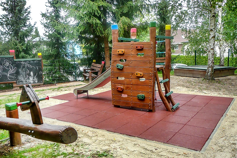 Fallschutz aus roten Fallschutzplatten rund um Kletterturm auf Spielplatz, wartungsfrei und stoßdämpfend.