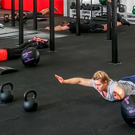 Le persone sdraiate sul pavimento scuro che si allenano in una palestra. Il pavimento è costituito da tappeti sportivi di protezione di WARCO.