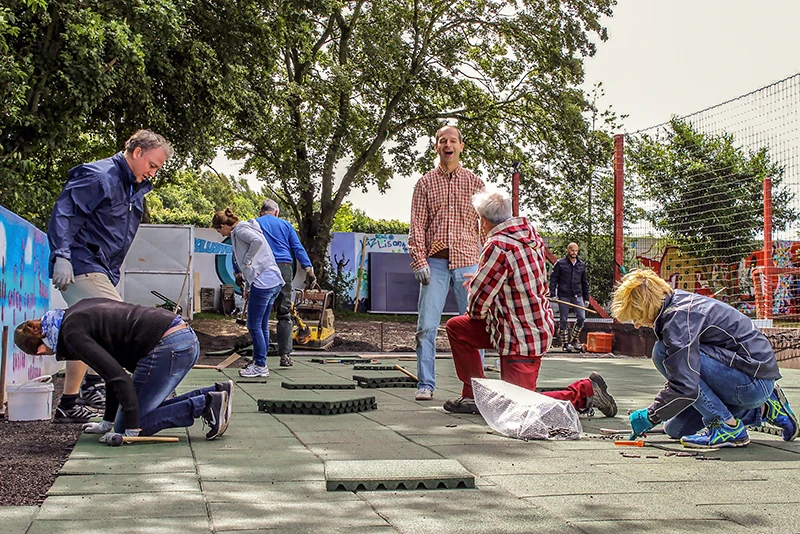 I genitori sorridenti installano personalmente le lastre antitrauma WARCO nel parco giochi della scuola dei loro figli.